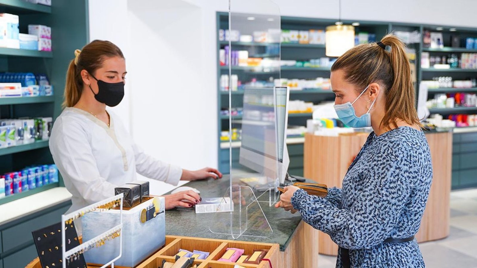 A Woman Wearing a Mask Receiving Medicine over the counter from a Woman Pharmacist 