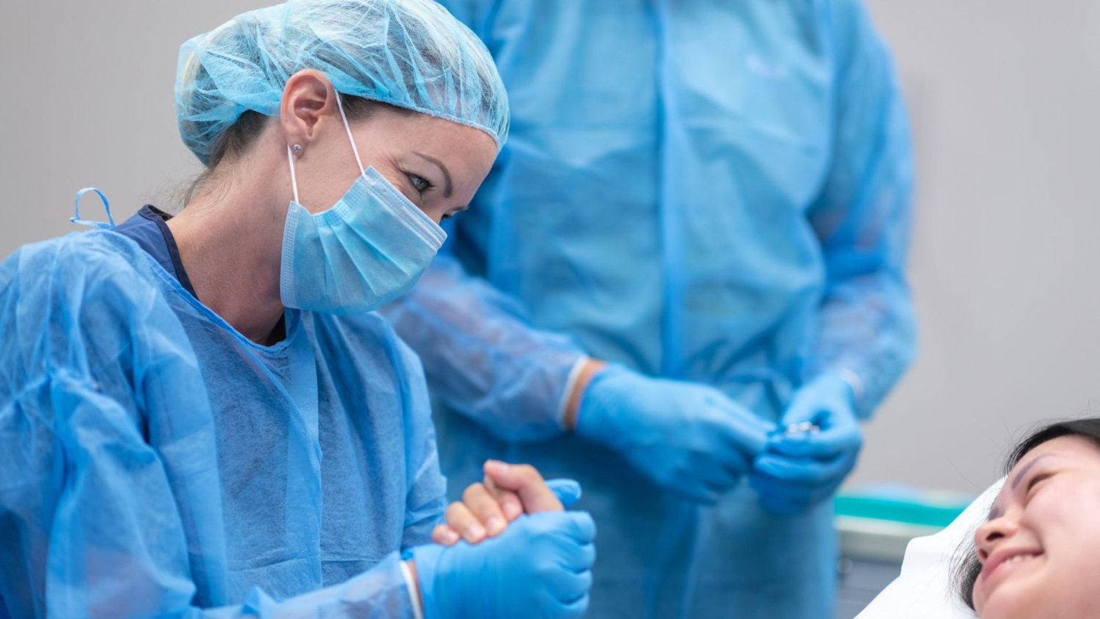 A Picture of a Doctor Wearing Blue SCrubs Holding a Patient 's Hand Whilst another Man Looks On 